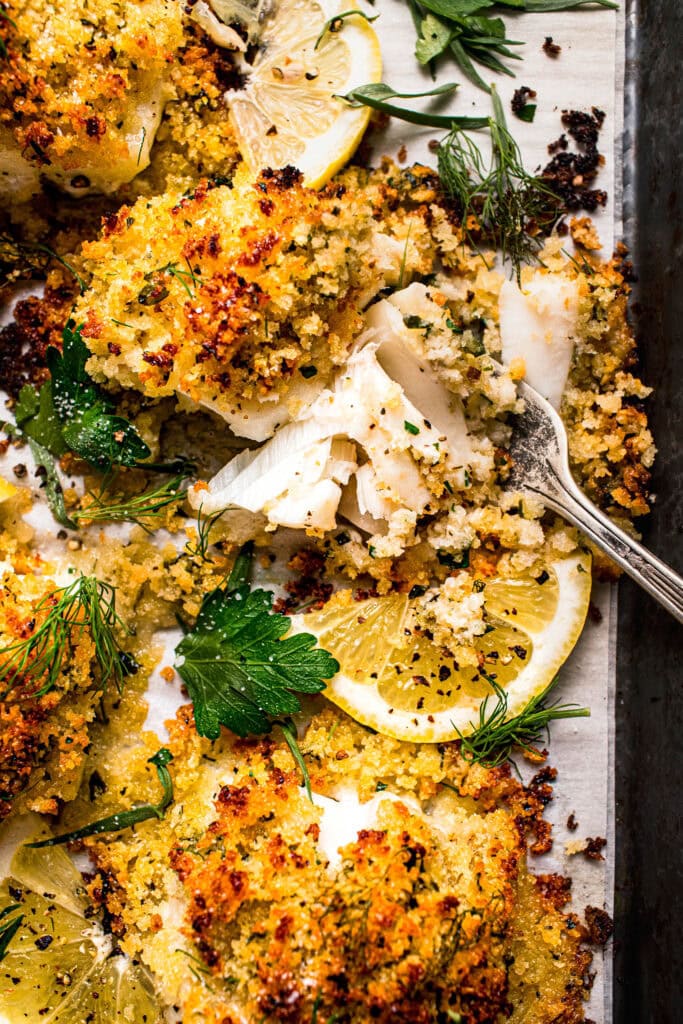 Pieces of baked panko cod arranged on baking sheet with fork. 