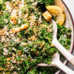 Overhead close up of simple kale salad in bowl with salad serving utensils.