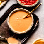 Creamy harissa sauce in small bowl next to spoon.