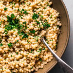 Overhead close up of pearl couscous in serving bowl topped with parsley.