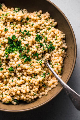 Overhead close up of pearl couscous in serving bowl topped with parsley.