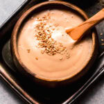 Overhead shot of sesame sauce swirled in bowl and topped with sesame seeds.