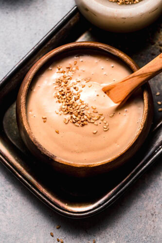 Overhead shot of sesame sauce swirled in bowl and topped with sesame seeds.