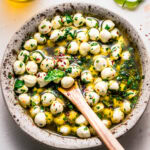 Overhead shot of marinated mozzarella balls in speckled bowl with wooden spoon.
