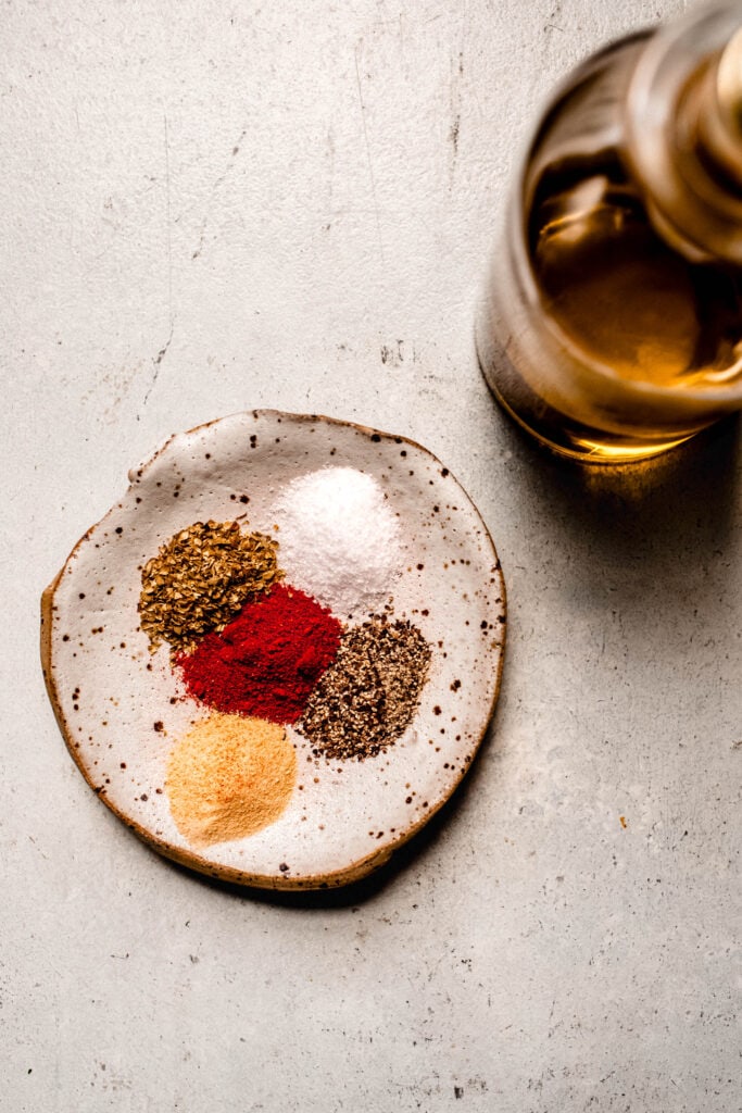Spices for air fryer chicken bites on small plate next to container of oil.