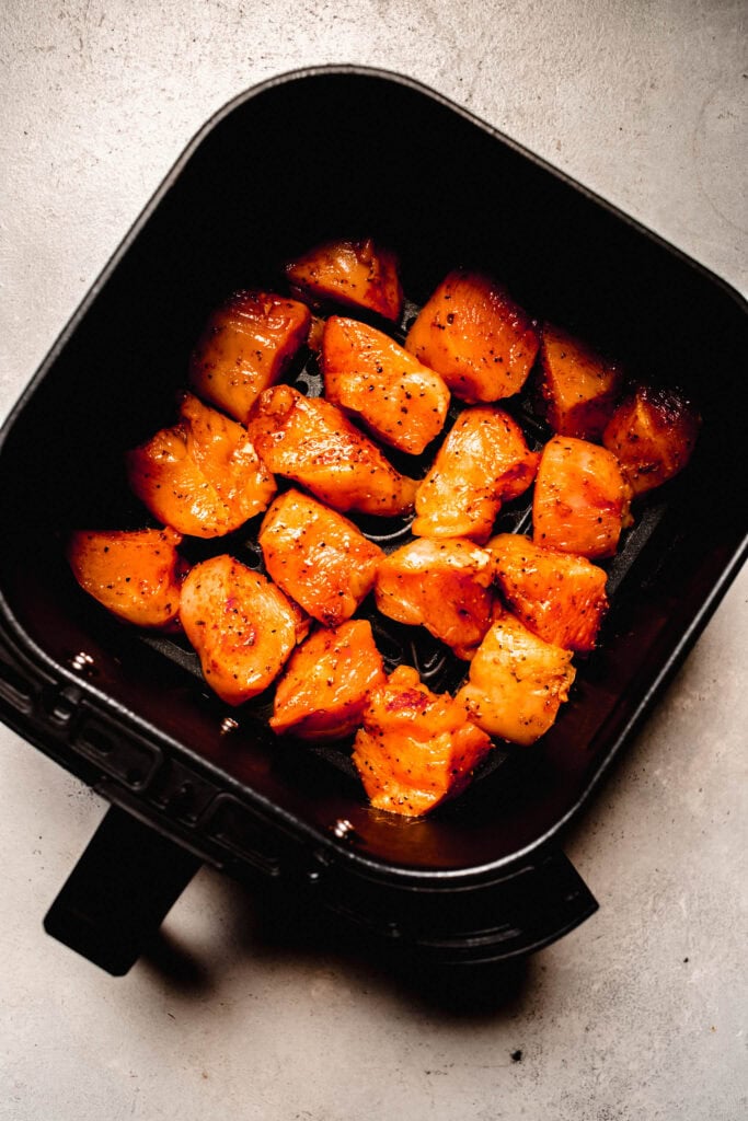 Raw chicken bites in air fryer basket.