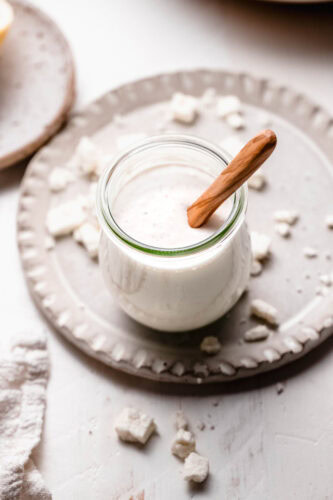 Creamy feta dressing in small glass jar with wooden spoon.