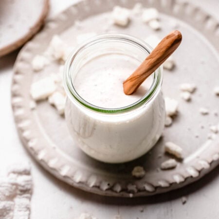 Creamy feta dressing in small glass jar with wooden spoon.