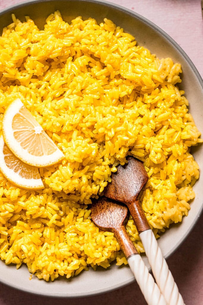 Overhead close up of greek lemon rice in bowl with serving spoons.