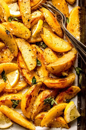 Greek roasted potatoes on baking sheet sprinkled with fresh oregano and lemon wedges.