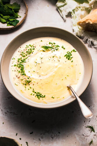 Side view of bowl of healthy potato leek soup next to piece of bread.