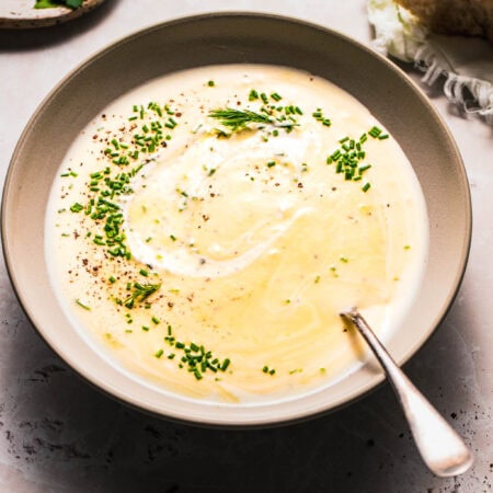 Side view of bowl of healthy potato leek soup next to piece of bread.