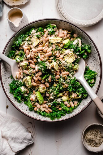 Kale and white bean salad in large speckled serving bowl on white wood counter.