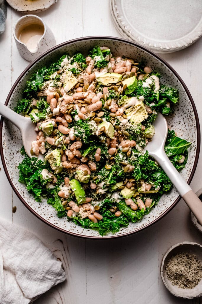 Kale and white bean salad in large speckled serving bowl on white wood counter.