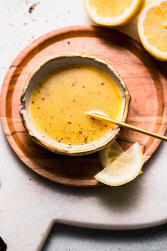 Lemon pepper in small bowl with gold spoon next to lemon wedges.