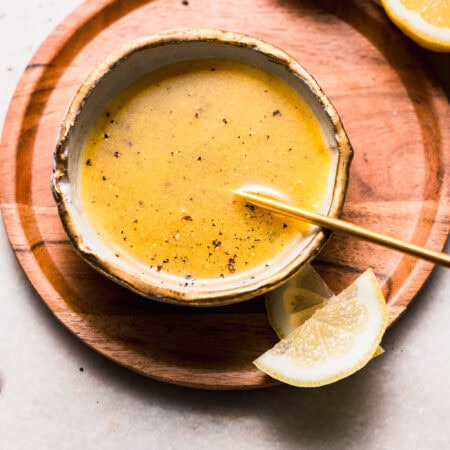 Lemon pepper in small bowl with gold spoon next to lemon wedges.