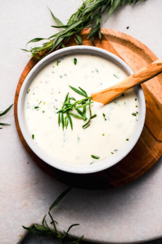 Creamy tarragon sauce in white bowl with wooden spoon.