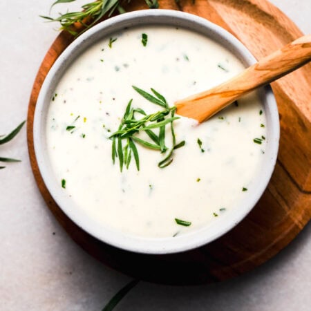 Creamy tarragon sauce in white bowl with wooden spoon.