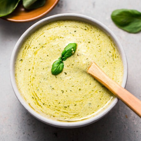 Pesto cream sauce in small white bowl topped with sprig of basil.