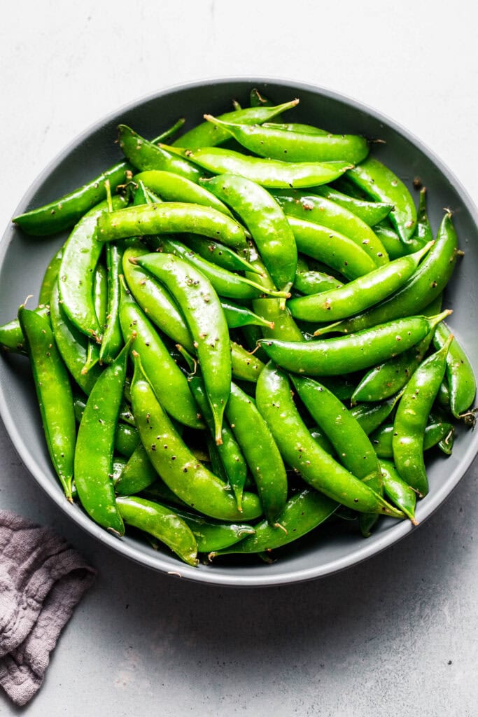 Overhead shot of bowl of sauteed snap peas in grey bowl.