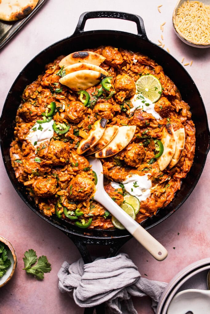 Butter chicken meatballs and orzo in skillet with serving spoon.
