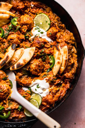 Overhead close up of Butter chicken meatballs and orzo in skillet with serving spoon.