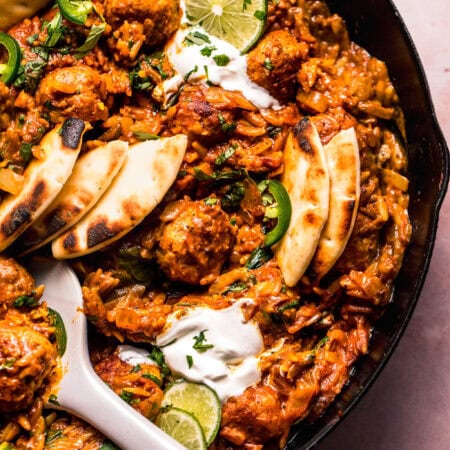Overhead close up of Butter chicken meatballs and orzo in skillet with serving spoon.