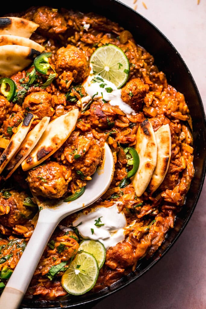 Overhead close up of Butter chicken meatballs and orzo in skillet with serving spoon.