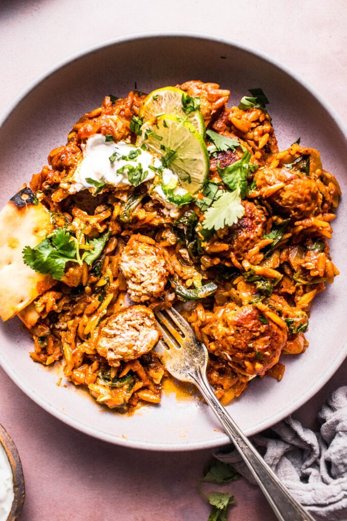 Overhead close up of butter chicken orzo in serving bowl with fork and meatball sliced into.