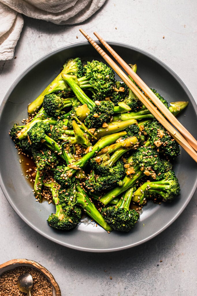 Overhead shot of broccoli stir fry in grey bowl with chopsticks.