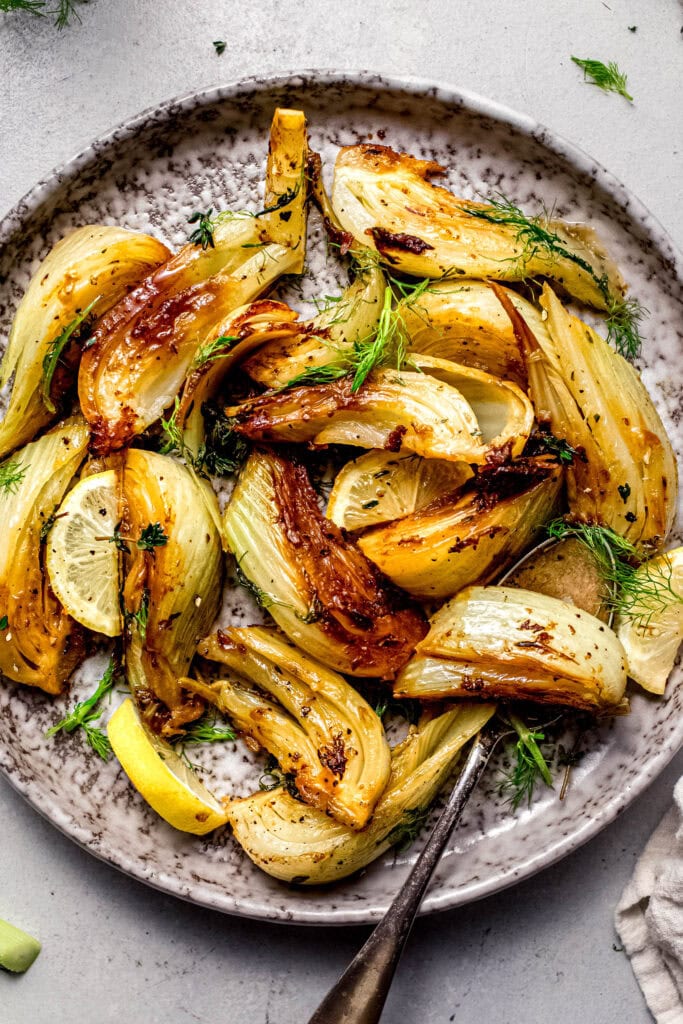 Braised fennel arranged on grey plate with lemon wedges and fennel fronds.
