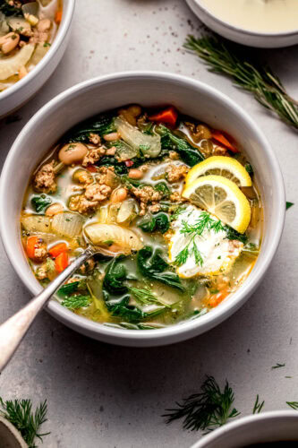Side view of lemony turkey bean soup in bowl topped with lemon wedges and dollop of sour cream.