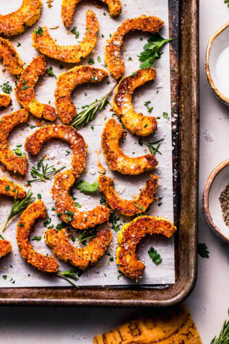 Finished roasted parmesan squash pieces on baking sheet with sprigs of rosemary.