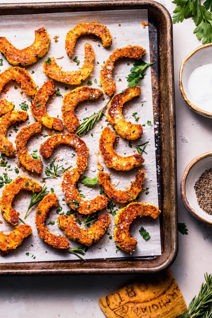 Finished roasted parmesan squash pieces on baking sheet with sprigs of rosemary.