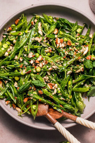 Overhead close up of snap pea salad in pink bowl on pink background ready to be served.