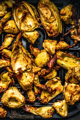 Close up of crispy artichoke hearts in air fryer basket.