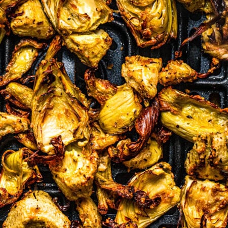 Close up of crispy artichoke hearts in air fryer basket.