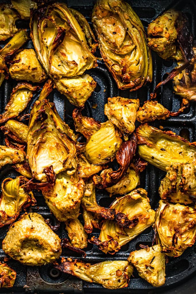 Close up of crispy artichoke hearts in air fryer basket. 