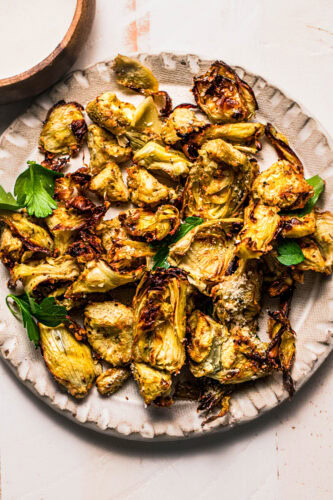 Air fried artichoke hearts on white plate with parsley leaves.