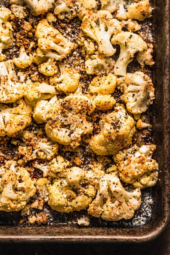 Roasted cacio e pepe cauliflower florets on baking sheet sprinkled with coarsed pepper and romano cheese.
