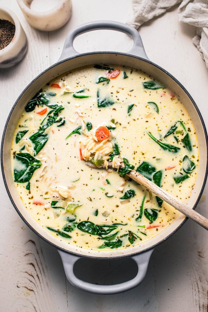 Creamy orzo chicken soup in large pot with wooden spoon.