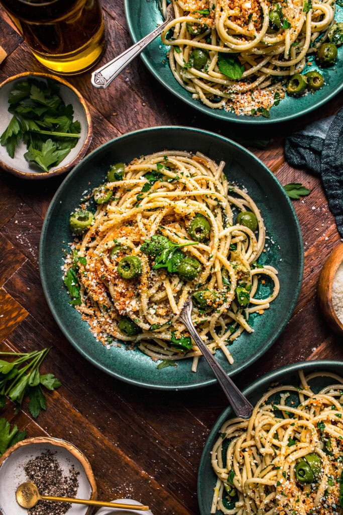 Three bowls of green olive pasta in green bowls next to small bowls of toppings.