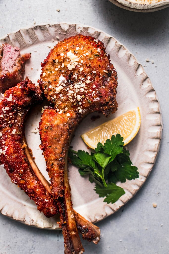 Close up of two parmesan crusted lamb chops on serving plate.