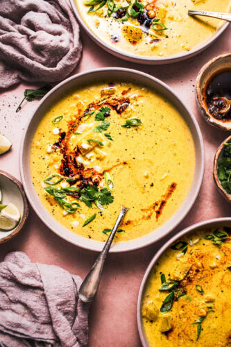 THREE BOWLS OF CURRY CORN CHOWDER DRIZZLED WITH CHILI CRISP AND SPRINKLED WITH GREEN ONIONS.