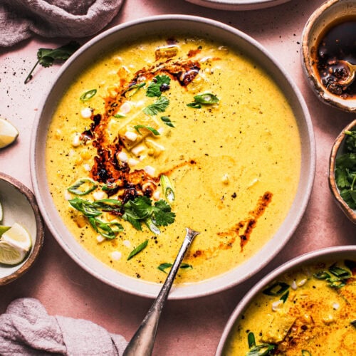 THREE BOWLS OF CURRY CORN CHOWDER DRIZZLED WITH CHILI CRISP AND SPRINKLED WITH GREEN ONIONS.