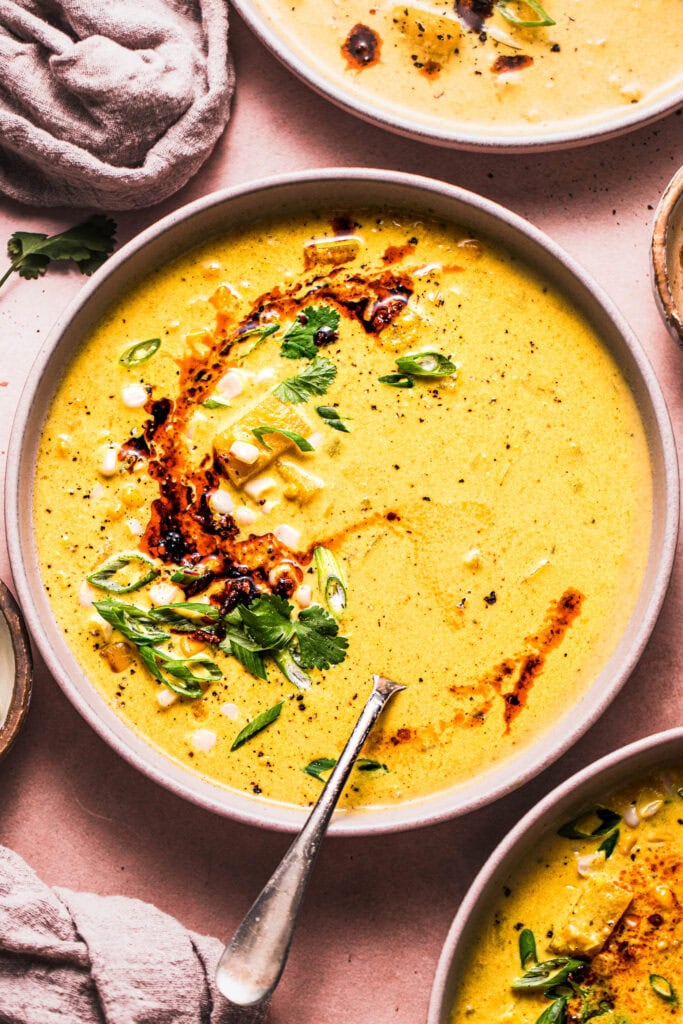 OVERHEAD CLOSE UP OF BOWL OF CURRY CORN CHOWDER ON PINK TABLE. 