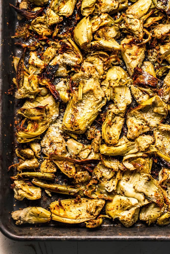 Close up of roasted and seasoned artichoke hearts on baking sheet.