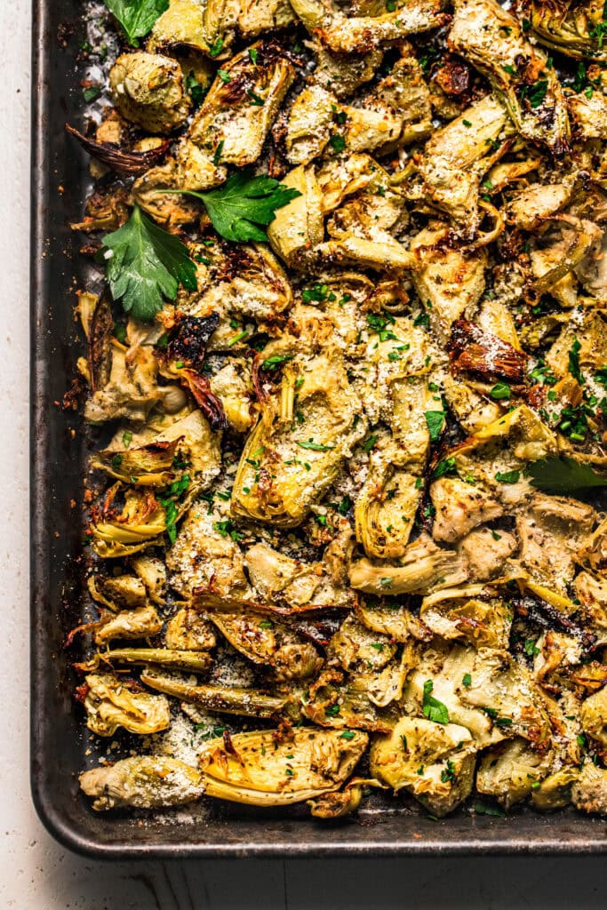 Finished seasoned and roasted artichoke hearts on baking sheet with parsley leaves.