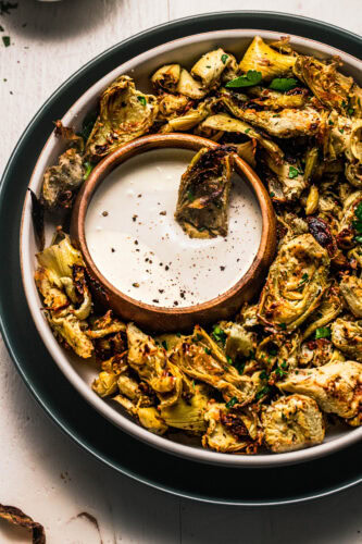 Roasted artichoke hearts arranged on plate with dipping sauce.