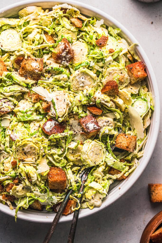 Overhead close up of prepared brussel sprout caesar salad in white bowl. 